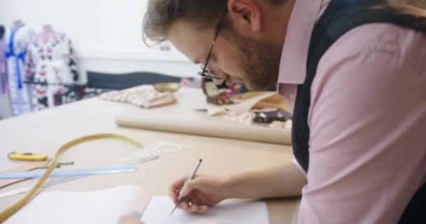 Sastre con gafas dibuja patrones de costura en cuaderno de bocetos — Vídeos de Stock