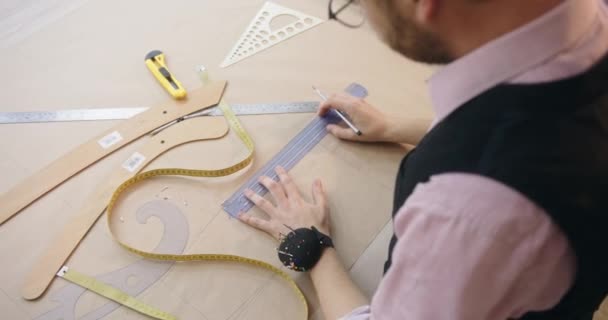 Kleermaker met potlood en liniaal tekent naaipatronen op stof — Stockvideo