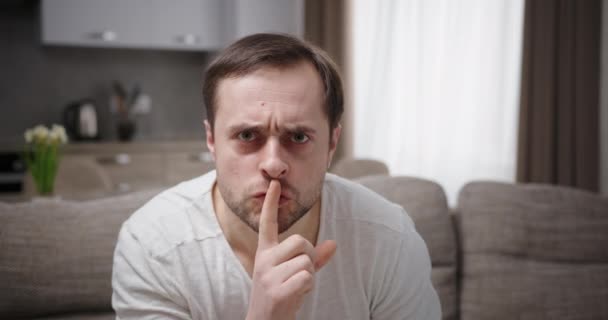Człowiek negatywnie zły, zmartwiony hałasem inaczej pokazuje gest po cichu przyciskając palec do ust, siedząc w domu na kanapie. — Wideo stockowe