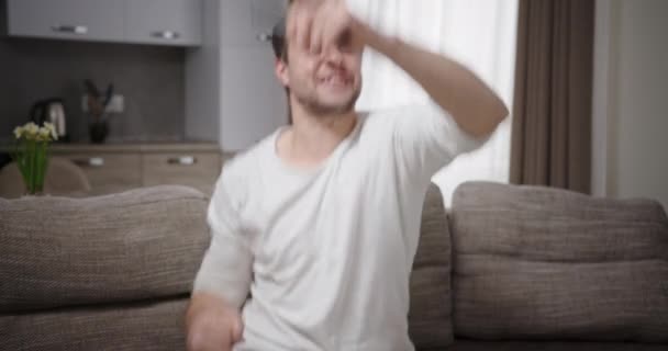 El hombre mira el teléfono y se regocija en ganar el juego divertido bailando feliz mueve sus manos sonriendo sentado en casa en el sofá — Vídeo de stock