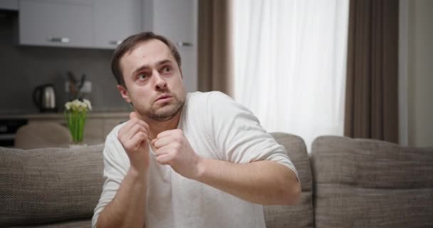 A man watching a horror movie is very scared shudders covers his face with his hands feels horror and fear sitting at home on the couch — Stock Video