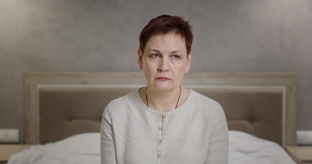 Mujer con corte de pelo corto sentada en la cama en casa preocupada escucha voces en su cabeza deprimida siente dolor de cabeza y desesperación — Vídeos de Stock