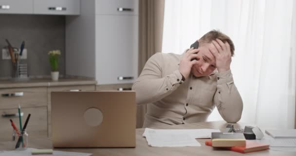 Hombre trabajando en casa sentado en su escritorio hablando por teléfono conversación desagradable molesto sosteniendo su cabeza se siente deprimido crisis — Vídeos de Stock