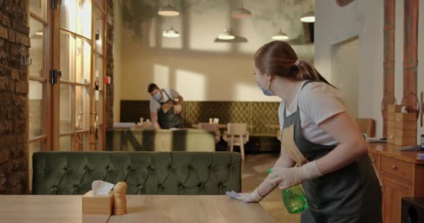 Pulizia disinfezione dei tavoli in un caffè due camerieri una ragazza e un ragazzo pulire i tavoli in un istituto chiuso in guanti mascherati — Video Stock