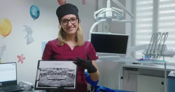 Zahnärztin Frau blickt positiv lächelnd in Kamera und zeigt Röntgenbild der Zähne von Patientinnen — Stockvideo