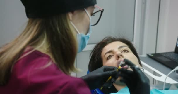 O processo de colocar faixas de borracha coloridas para ligaduras ligaduras mulher paciente amarelo deitado com a boca aberta em uma cadeira dentária — Vídeo de Stock