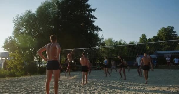 Team van vrienden spelen beach volleybal competitie een man verslaan van de bal spelen bij zonsondergang op het zand zomer waterfront — Stockvideo