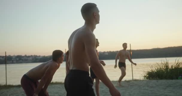 Strandvolleybal spelen verschillende generaties jonge en oude mannen spelen actieve tijd in de zomer op de zonsondergang aan het water — Stockvideo