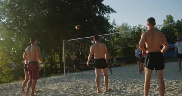 Aktywny mecz siatkówki rekreacyjnej 2 drużyny konkurować na wybrzeżu jazdy na piasku w letni zachód słońca — Wideo stockowe