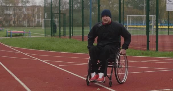 Ancien athlète après blessure Athlète handicapé homme aux jambes défectueuses chevauchant en fauteuil roulant dans la rue du stade à l'extérieur vêtu de vêtements de sport — Video