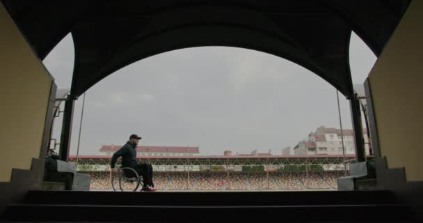 Ex atleta discapacitado en una silla de ruedas paseos en el estadio recuerda nostálgico pierde silueta en la calle fuera después de una lesión en la pierna atleta discapacitado. — Vídeo de stock