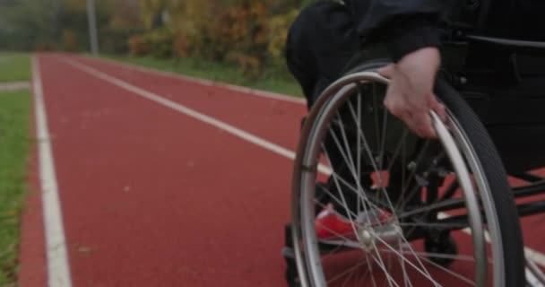 Анонимный спортсмен-инвалид с дефектными ногами едет в инвалидной коляске по улице стадиона на улице одетый в спортивную одежду бывший спортсмен — стоковое видео