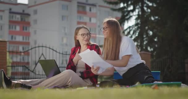 Gelukkige vriendinnen maken huiswerk in park — Stockvideo