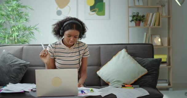 美しい暗い肌のアフリカ系アメリカ人のかなりの女性学生は、コンピュータ画面を見て、ウェビナーを閲覧したり、ウェブカメラとビデオチャットをしています。家に座っている間にアイデアの錫を表示します。 — ストック動画