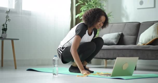 Preto africano americano menina treina online olha para laptop e repete ioga exercícios sentado no tapete em casa — Vídeo de Stock