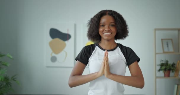 Vacker ung mörkhyad afroamerikansk kvinna med lockigt hår tittar på kameran leende vikta armarna framför sin yoga hemma — Stockvideo