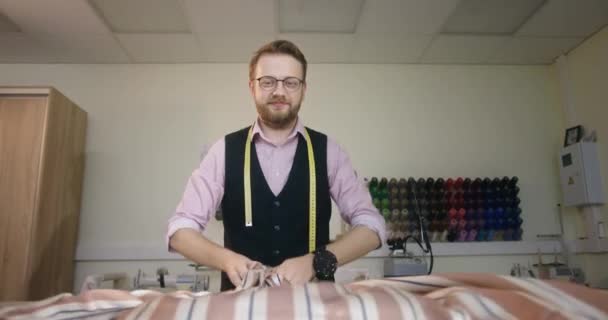 Un joven diseñador de moda sonriente se para en su taller lanza una tela para un futuro producto cubre la cámara — Vídeo de stock