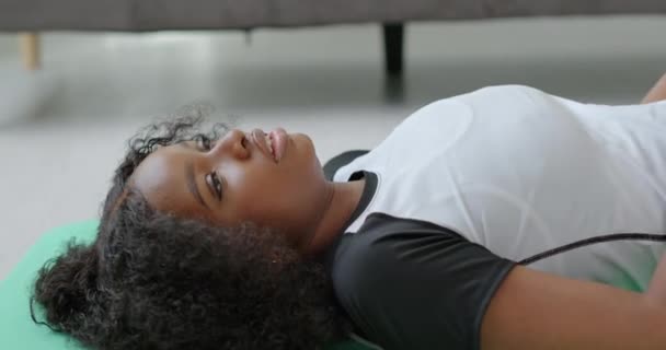 美しい黒人アフリカ系アメリカ人の女の子が地面に横たわっていますカメラを見て笑顔を訓練した後、深い呼吸を取ります — ストック動画