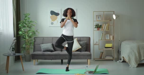 Ejercicio de yoga Namaste Chica afroamericana negra haciendo ejercicio en casa de pie en una pierna mirando a la cámara y sonriendo — Vídeos de Stock