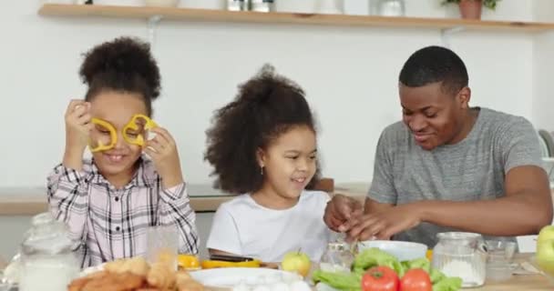 Famiglia dalla pelle scura di afro-papà e afro-americano ragazze bambini sorelle insieme positivamente cucinare insieme stupidamente scherzare verdure invece di occhi cucina a casa — Video Stock