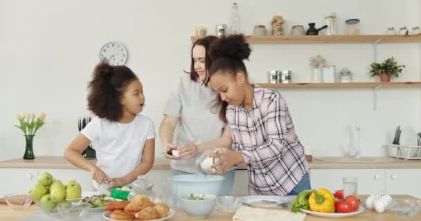 Famille multiraciale mère blanche et filles afro-américaines enfants sœurs amicales embrasser positivement embrasser ensemble cuisine salade à la maison dans la cuisine — Video