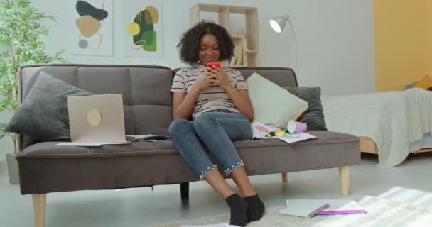 Afroamerikanische Studentin nutzt Smartphone auf Couch — Stockvideo