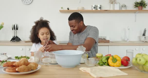 お父さんと娘の料理暗い肌の家族アフロパパとアフリカ系アメリカ人の女の子子供たち一緒に積極的に一緒に台所のお父さんで家に砂糖を注ぐ料理を調理することは娘を助ける — ストック動画