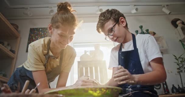 Pottery master class žena učí mladý dospívající chlapec pracující společně při pohledu na sebe usměvavý sedí za hrnčíř kolo vytváří hliněný produkt — Stock video