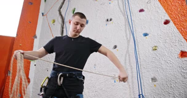 Tekercselő kötél, egy fiatal srác mászik, áll a háttérben egy mesterséges fal mászás csavar remény kötél — Stock videók