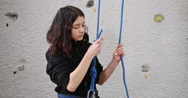 Девушка лазает по искусственной стене проверяет страховку веревку, глядя в камеру улыбающийся портрет — стоковое видео