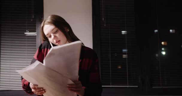 Женщина с документами разговаривает на смартфоне в офисе поздно вечером — стоковое видео