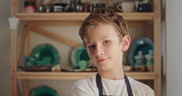 Glimlachende jongen in schort en bril in aardewerk werkplaats — Stockvideo