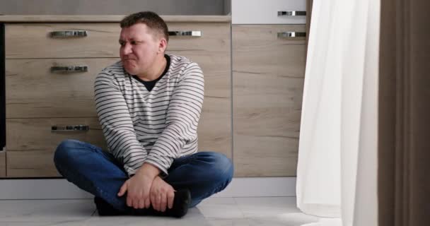 Anxious man sitting on floor in kitchen — Stock Video