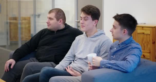 Team af unge fyre sidder på sofaen i moderne kontor følelsesmæssigt diskutere nyt projekt smilende griner gestikulerende hænder – Stock-video