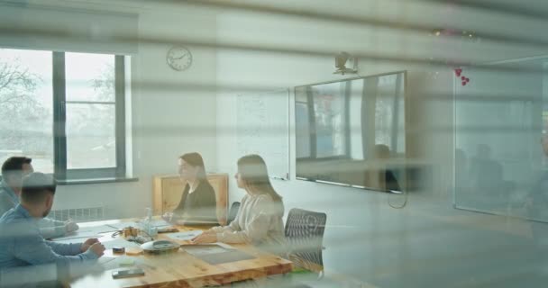 Chica cierra persianas en la oficina Un equipo de jóvenes que trabajan juntos en una empresa en una oficina moderna sentados en una mesa de negociación discutiendo un nuevo proyecto — Vídeo de stock