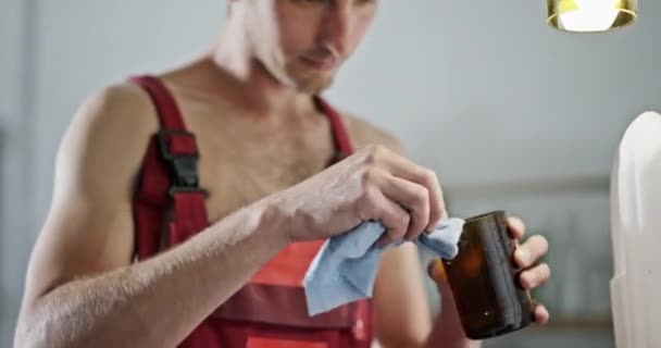 De jongeman maakt een glas van de bewerkte glazen flessen het ecologische project staat in de creatieve werkplaats in speciale kleding — Stockvideo