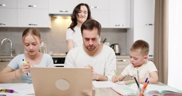 Cansado homem tenta trabalhar no laptop com crianças na cozinha — Vídeo de Stock