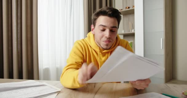 Funny man in yellow hoodie throws papers at wooden table — Stock Video