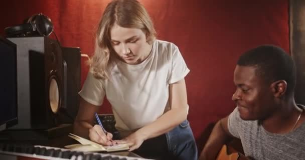 Mujer escribe en cuaderno hombre afroamericano toca la guitarra — Vídeo de stock