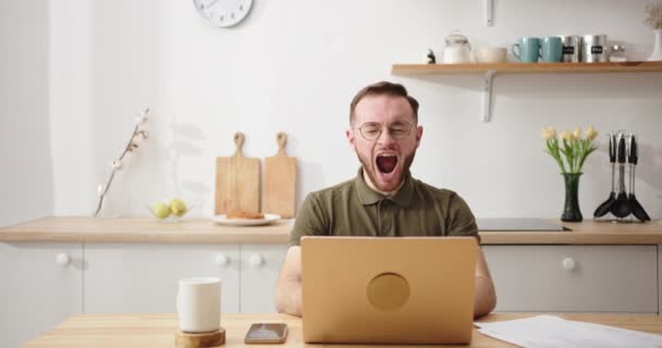 Ospalý mladý muž s brýlemi unavený běží v noci sedí doma v kuchyni u stolu pracuje na notebook zívání chce spát se snaží neusnout — Stock video