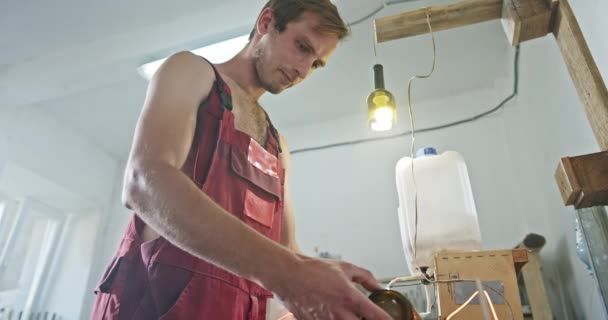 Het ecologische project staat aan het gereedschap in de creatieve werkplaats in speciale kleding De jongeman houdt zich bezig met de verwerking van glazen flessen — Stockvideo