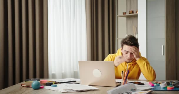 Junger Mann, der zu Hause im Homeoffice arbeitet, sitzt am Schreibtisch und arbeitet an einem Laptop. Von Überstunden müde, spürt er Nackenschmerzen und Erschöpfung — Stockvideo