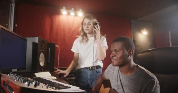 Muziek maken in een muziekstudio Multiraciale muziek band meisje in koptelefoon opnemen en afro-Amerikaanse muzikant gitarist spelen — Stockvideo