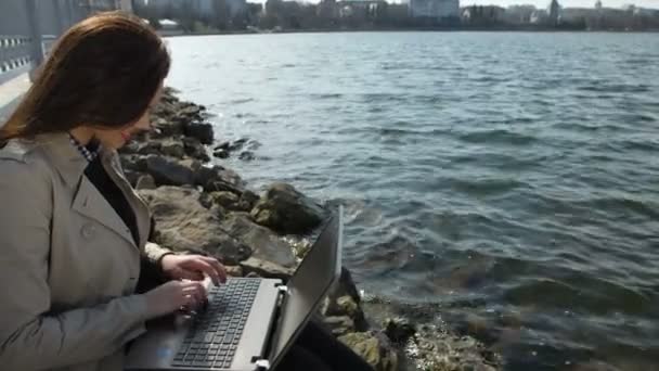 Iş kadını deniz kıyısında bir plajda otururken dizüstü bilgisayar ile — Stok video