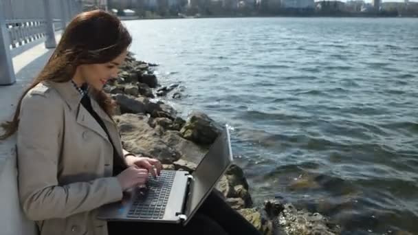 Mutlu bir iş kadını kumsalda oturan bir dizüstü bilgisayar ile — Stok video