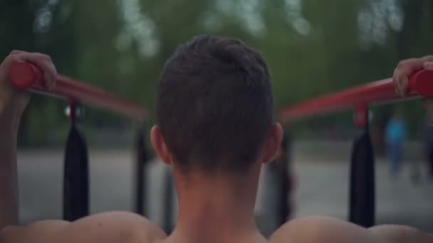 Mladý sportovec dělá cvičení na bradlech na hřišti večer. — Stock video