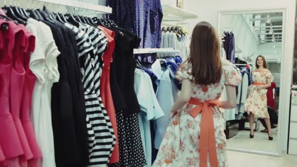 Молодая женщина выбирает одежду в выставочном зале — стоковое видео