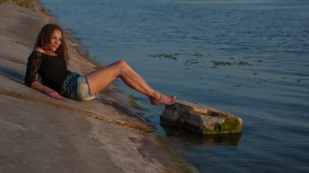 Beautiful girl in short shorts lying near the water — Stock Video