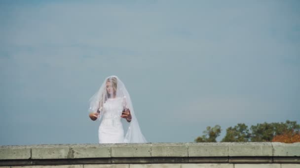 Gyönyörű menyasszony áll a falon egy elbűvölő fehér menyasszonyi ruha — Stock videók