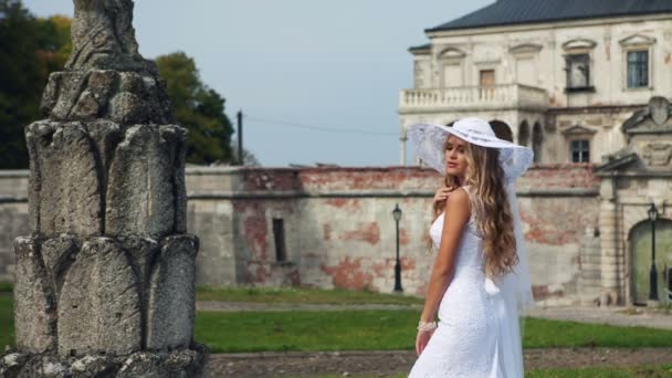 Blondynka w pięknej białej sukni i kapeluszu, w pobliżu starego zamku. — Wideo stockowe